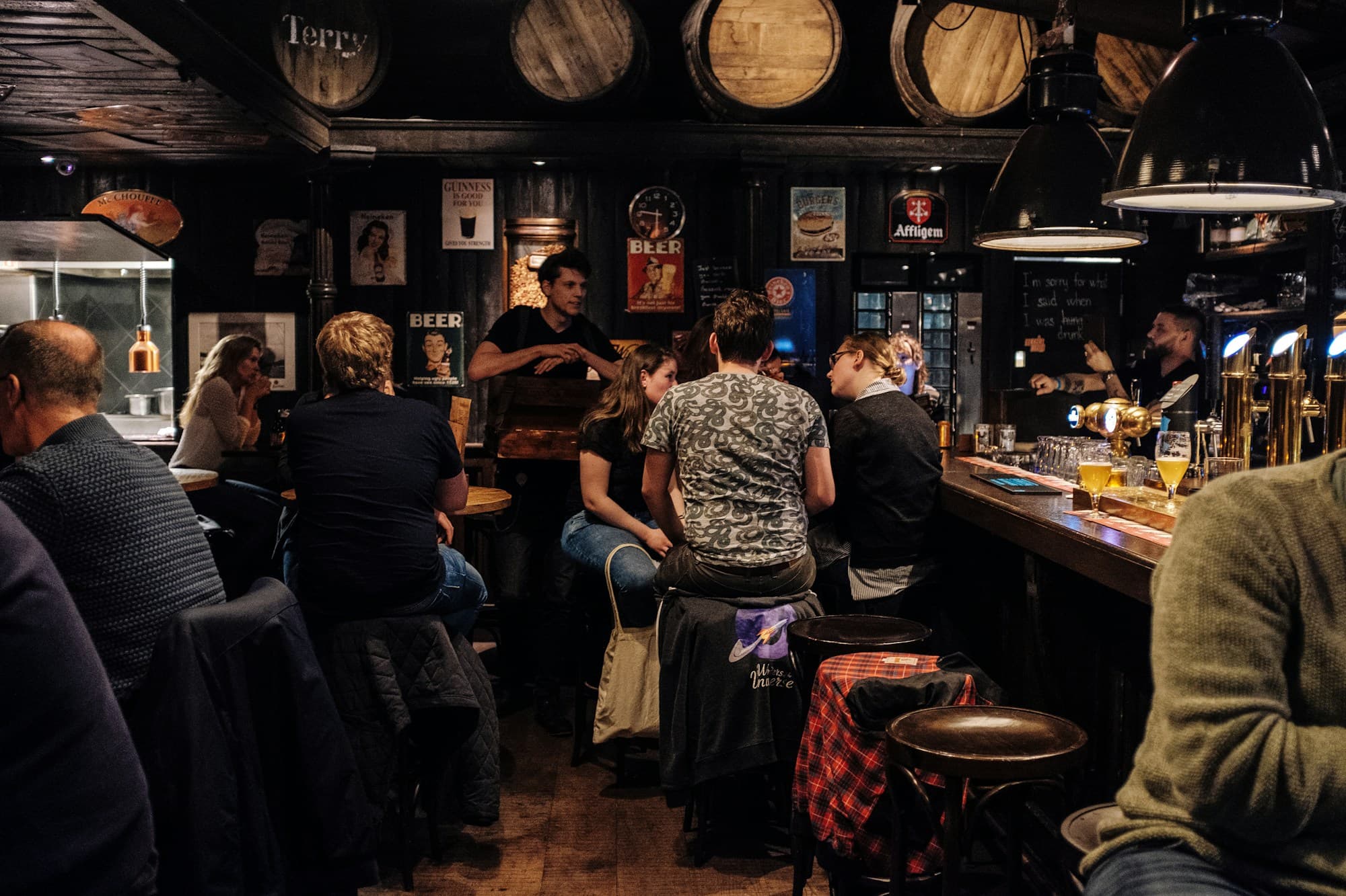 A busy neighbourhood bar in the evening, people at the counter and around tables